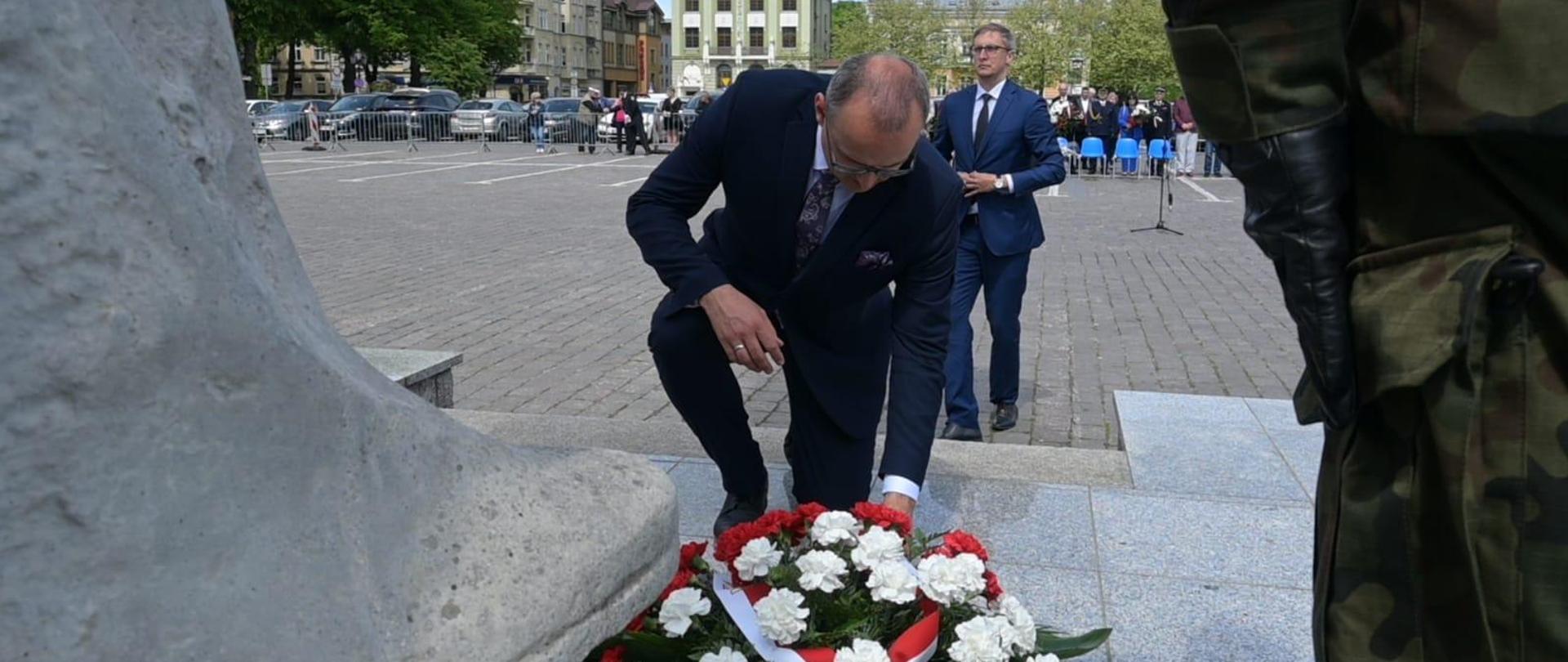 mężczyzna klęcząc składa wieniec pod pomnikiem 