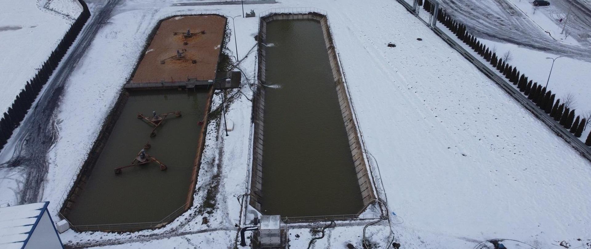 Widoczne zdjęcie z góry na oczyszczalnie ścieków i umieszczonym w pobliżu parkingiem. Wokół terenu znajduje się pokrywający śnieg.
