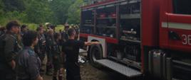 Zdajecie przedstawia strażaka z Jednostki Ratowniczo - Gaśniczej Dubiecko, który prezentuje uczestnikom kolonii sprzęt strażacki na samochodzie ratowniczym. W tle las