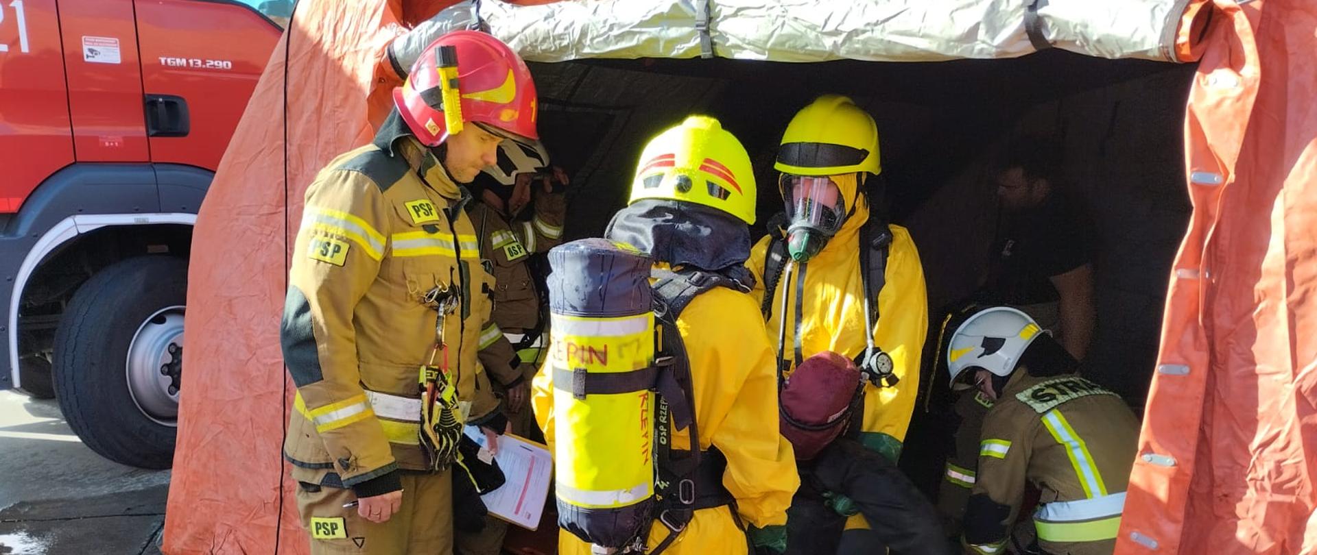 Strażacy w ubraniach ochrony chemicznej podczas ewakuacji manekina symulującego nieprzytomną osobę poszkodowaną.
