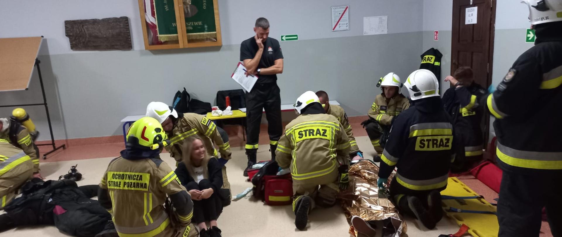 Zdjęcie przedstawia grupę strażaków podczas ćwiczeń. Ich prace ocenia jeden strażak