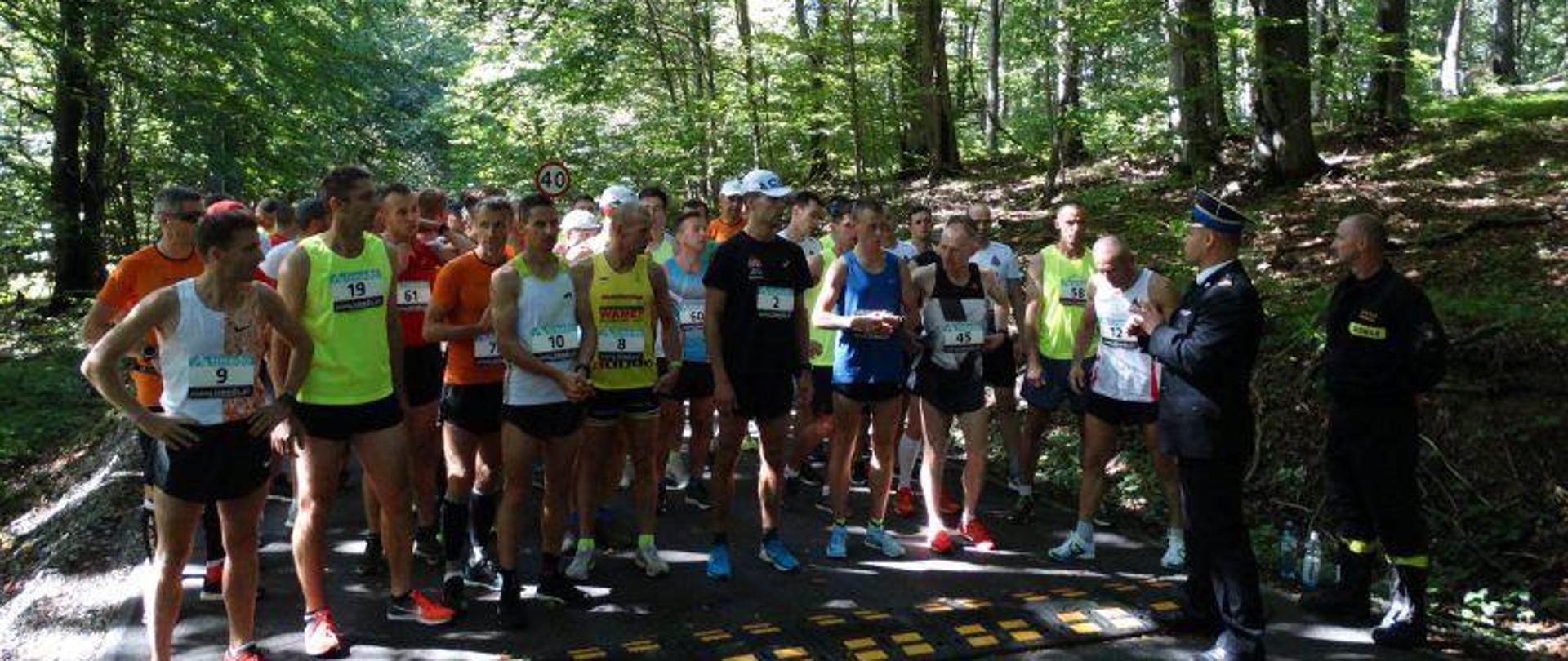 Zdjęcie przedstawiające uczestników stojących na starcie. W tle widoczne drzewa.