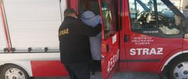 Zdjęcie przedstawia strażaka OSP w Górnem pomagającego kobiecie wejść do pojazdu pożarniczego w celu transportu do punktu szczepień