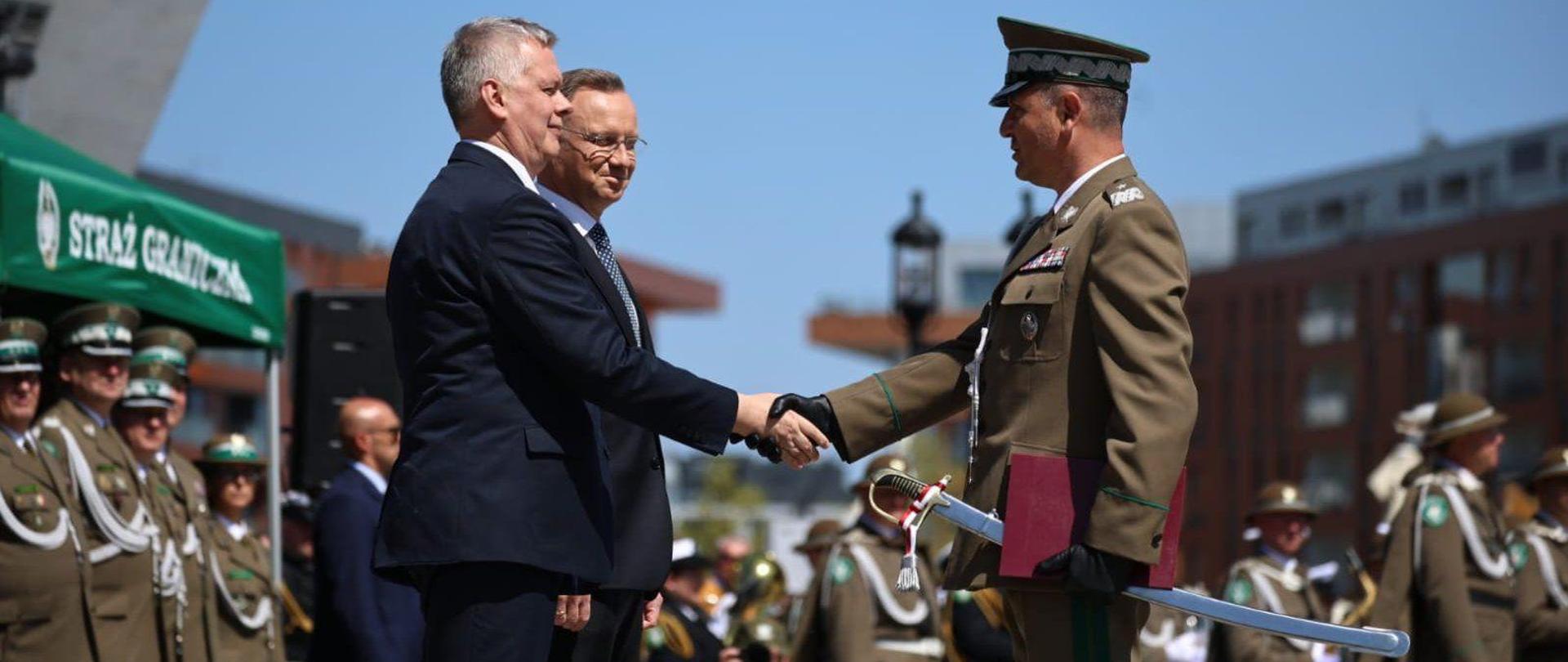 plac, na nim funkcjonariusze straży granicznej, na przodzie minister podaje rękę generałowi SG
