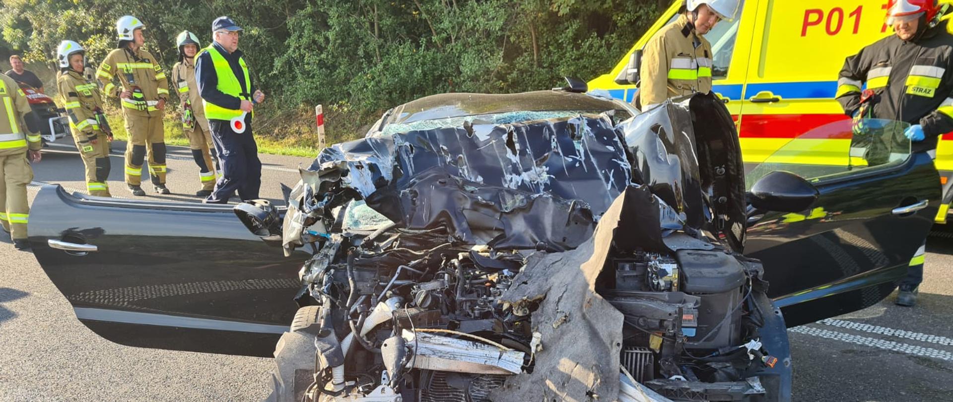 Na zdjęciu widzimy rozbity samochód osobowy oraz w tle Zespół Ratownictwa Medycznego