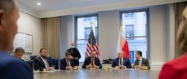 Przy okrągłym stole siedzą uczestnicy spotkania. Przy oknie siedzą wicepremier Jacek Sasin, prezes GPW Marek Dietl. W tle flagi Polski i USA.