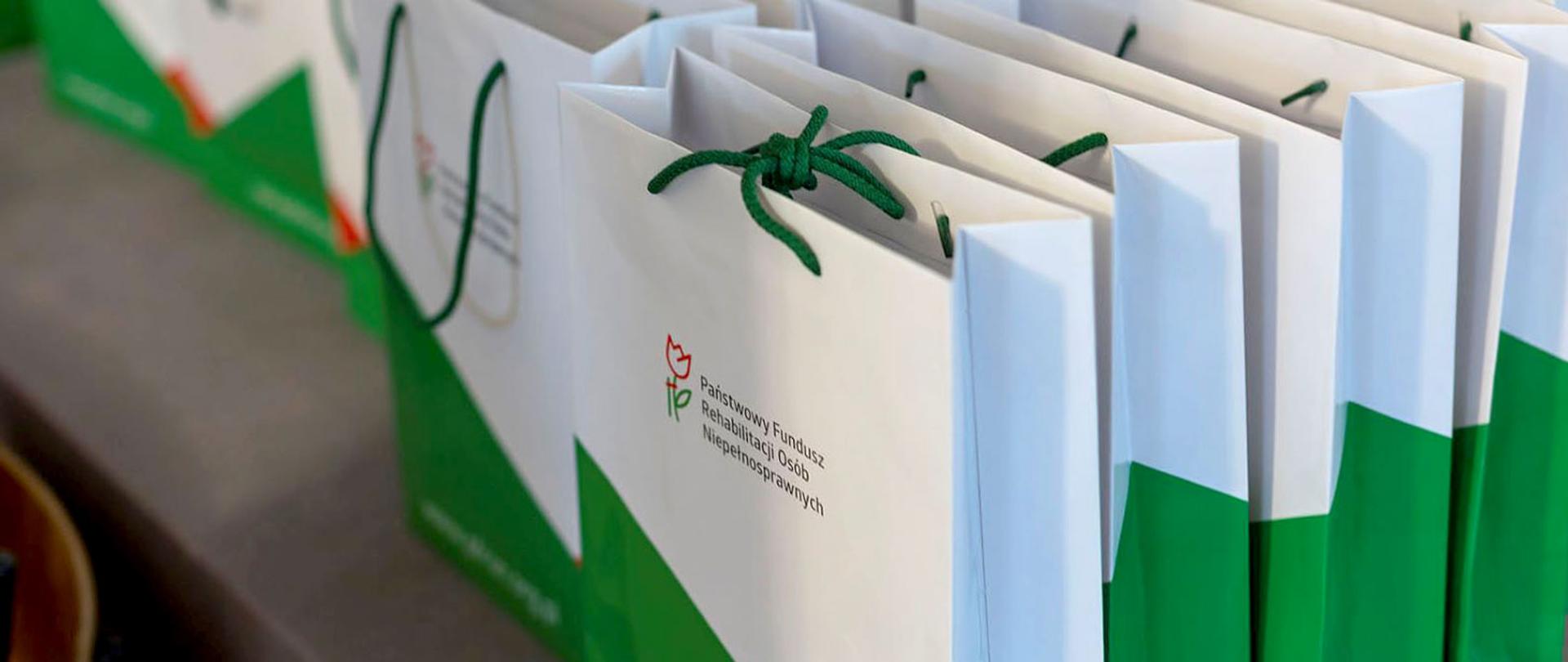 Na zdjęciu torby prezentowe z logiem Państwowego Funduszu Rehabilitacji Osób Niepełnosprawnych.