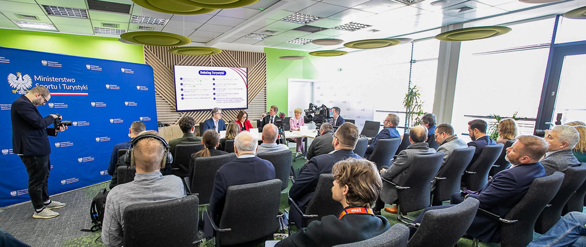 konferencja nt. deregulacji w hotelarstwie. Zdjęcie z konferencji, za stolikiem siedzi wiceminister sportu i turystyki oraz prezes Polskiej Organizacji Turystycznej