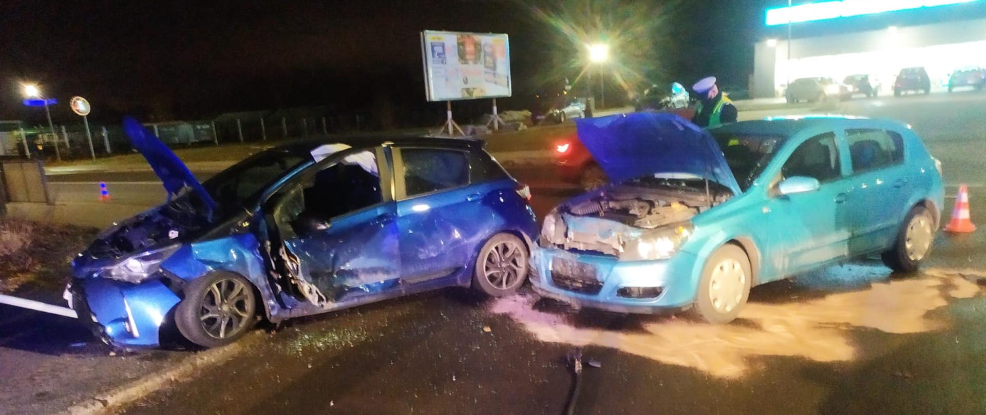 Na zdjęciu znajdują się dwa pojazdy po wypadku za nimi policjant prowadzący czynności