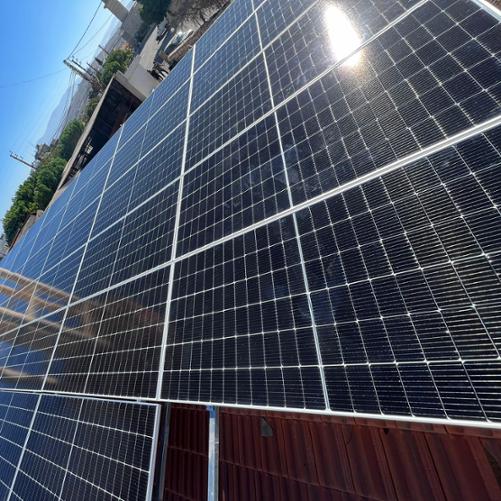 Panele fotowoltaiczne, na horyzoncie widać góry i zabudowania 