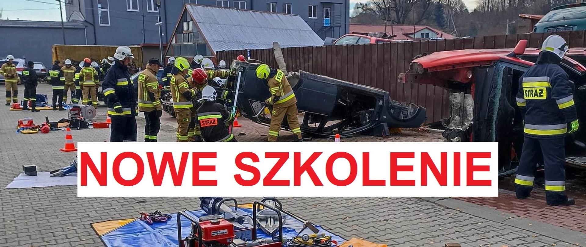 którym widać kilka grup umundurowanych na bojowo strażaków. Ćwiczą ze sprzętem ratowniczym przy kilku wrakach pojazdów. Sprzęt przygotowany i zgromadzonych na niebieskich matach przed wrakami. W tle widoczne częściowo zabudowania, ogrodzenie i szare drzewa. Na środku fotografii czerwony napis na białym tle o treści: nowe szkolenie.