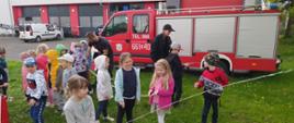 Na zdjęciu dzieci pod opieką strażaków bawią się podręcznym sprzętem strażackim