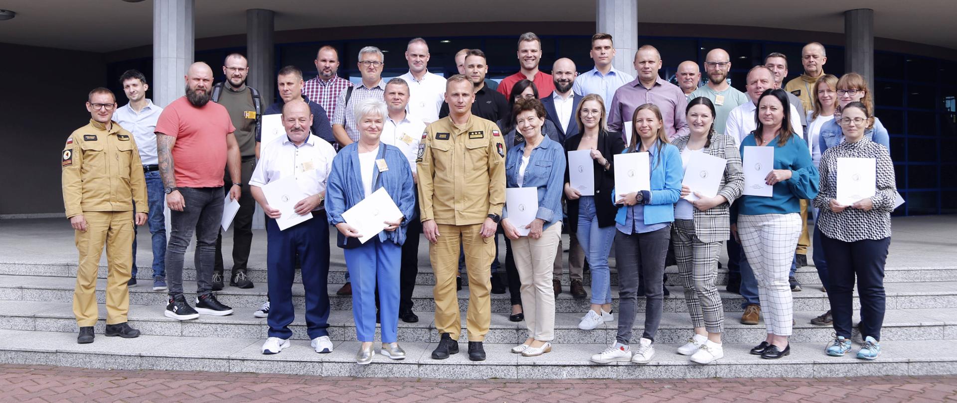 Grupowe zdjęcie uczestników szkolenia (28 osób) w towarzystwie Zastępcy Komendanta Centralnej Szkoły PSP, dwóch funkcjonariuszy CS PSP oraz kobiety