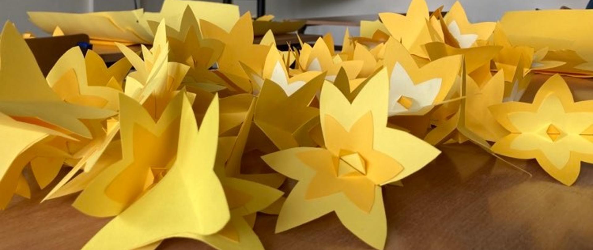 Na zdjęciu papierowe żonkile, w tle ekran monitora z instrukcją wykonania kwiatu