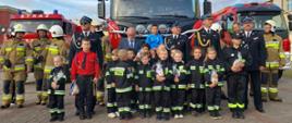Zdjęcie przedstawia strażaków, dzieci z dziecięcej drużyny pożarniczej oraz gości stojących na tle nowego samochodu ratowniczo-gaśniczego 