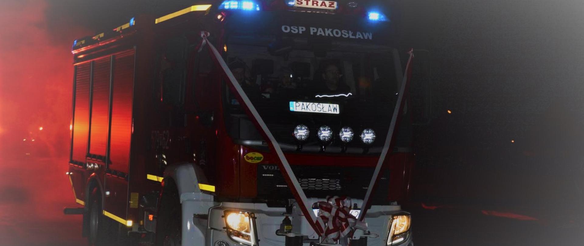 Wóz ratowniczo-gaśniczy, z przodu przystrojony biało-czerwonymi wstęgami oraz kokardą. Pojazd na dachu ma włączone niebieskie światła błyskowe oraz podświetlony napis "STRAŻ". W górnej części kabiny widnieje napis "OSP Pakosław", niżej "PAKOSŁAW". W kabinie dowódca i kierowca. Z lewej strony samochodu blask bijący od flar.