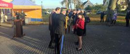 Pomorski komendant wojewódzki Państwowej Straży Pożarnej oddaje honor zaproszeni goście stoją przed przedstawicielami ochotniczej straży pożarnej. 