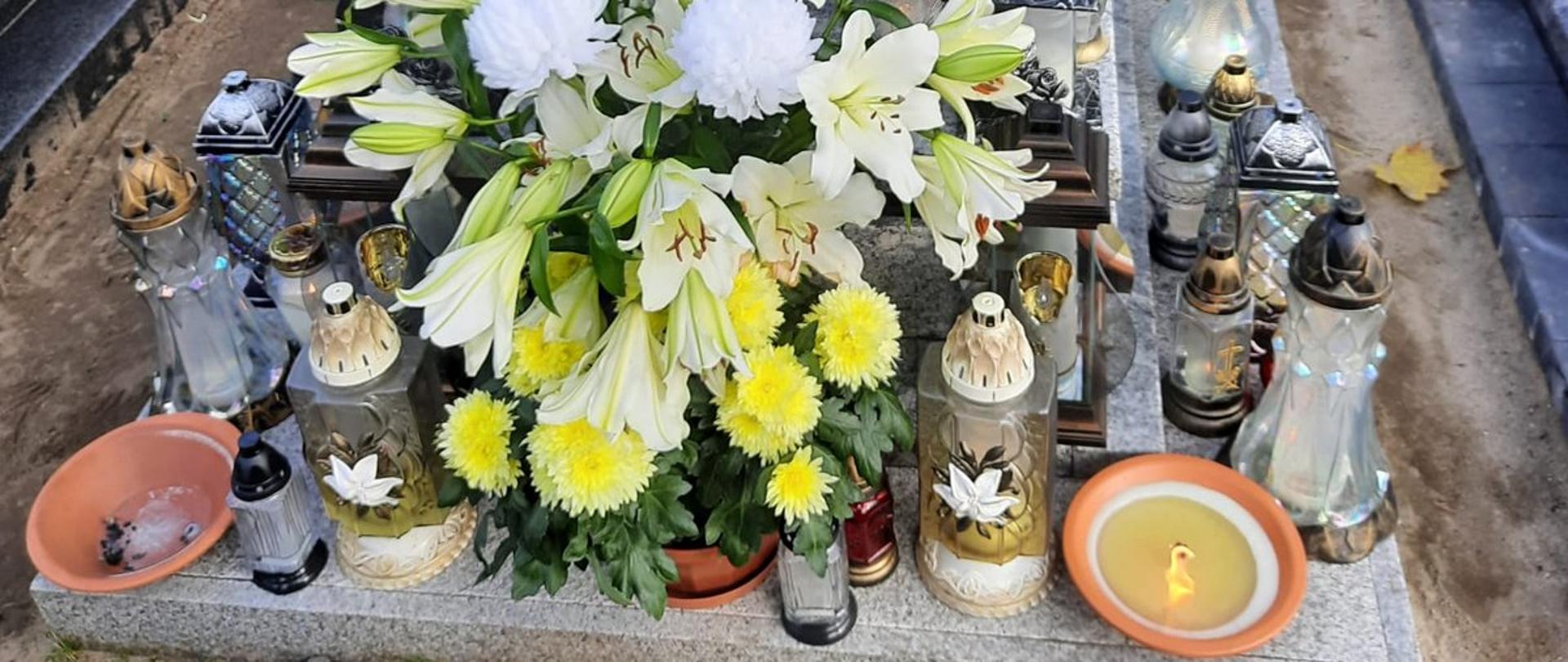 Zdjęcie przedstawia grób strażaka. Na grobie poustawiane są znicze oraz kwiaty.