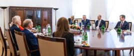 Zdjęcie przedstawia delegacje polską i estońską siedzące przy stole. U góry zdjęcia od prawej delegacja estońska – trzech mężczyzn i jedna kobieta (drugi od prawej siedzi minister Igor Taro). Z lewej strony zdjęcia delegacja polska – dwóch mężczyzn i dwie kobiety siedzące tyłem do obiektywu, drugi od lewej minister Tomasz Siemoniak. Na stole: termosy z kawą, filiżanki, szklanki, butelki z wodą, talerzyki z przekąskami. Na środku stołu kompozycja kwiatowa. W tle, po lewej stronie zdjęcia, duża, brązowa szafa oraz dwie lampy stojące. U góry zdjęcia widać fragment żyrandola. Po prawej stronie w tle dwa okna z białymi zasłonami. 