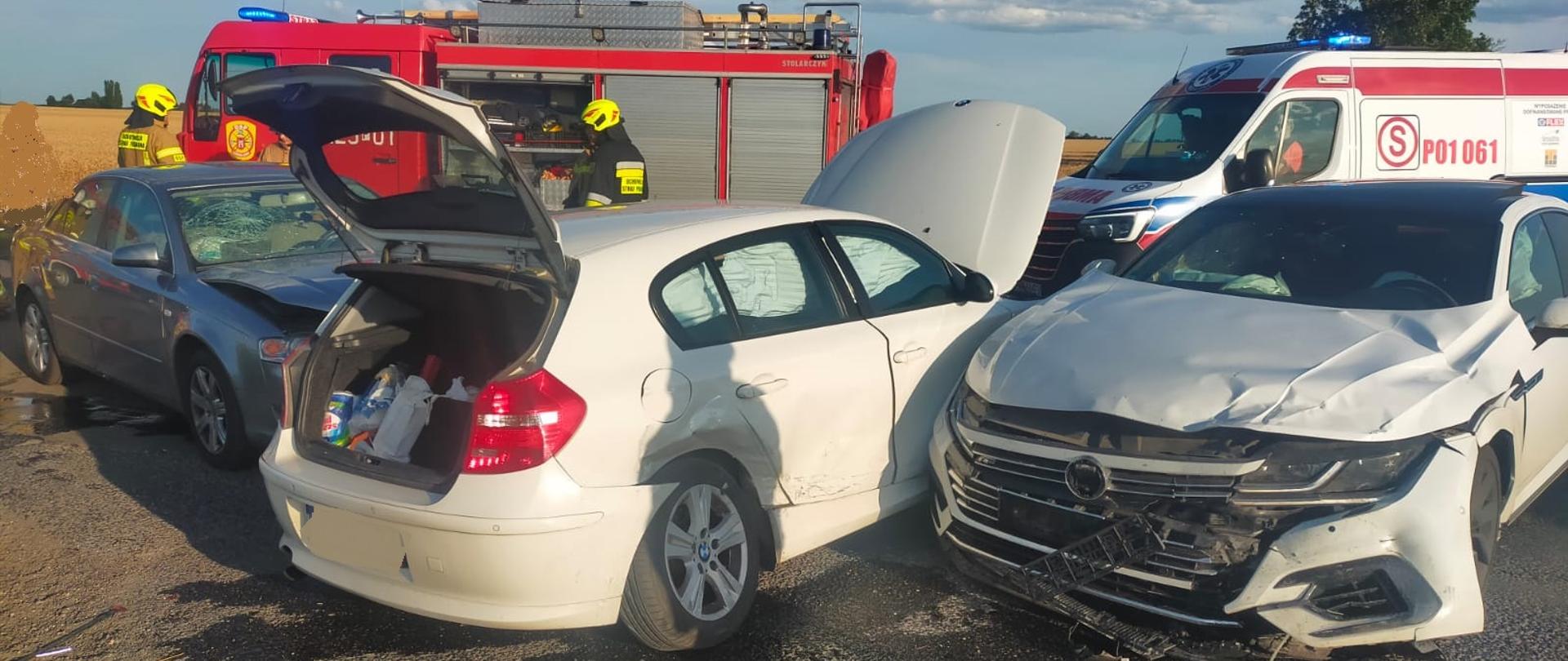 Na zdjęciu widać trzy samochody osobowe po kolizji. W tle za nimi stoi samochód pożarniczy oraz karetka pogotowia