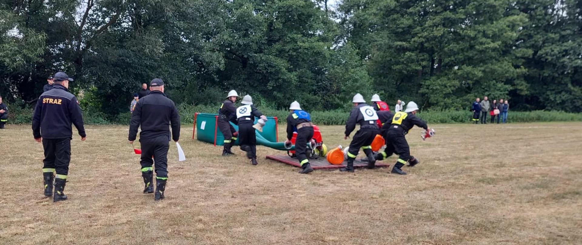 Strażacy w trakcie wykonywania ćwiczenia bojowego, biorą sprzęt z podestu.