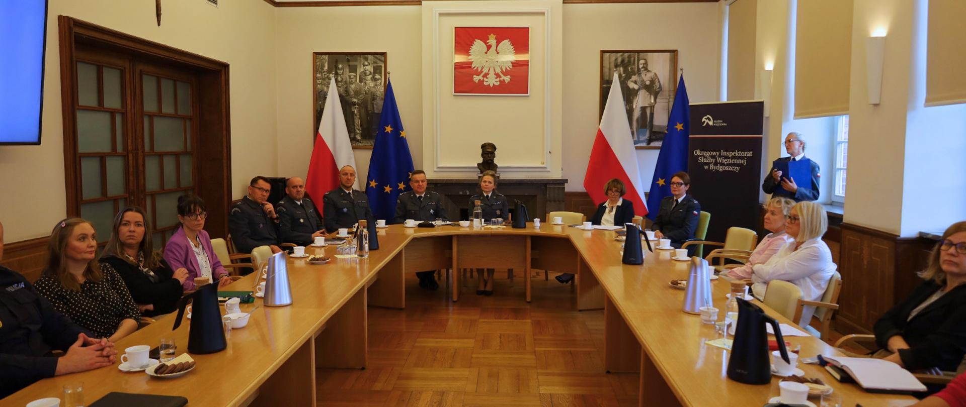 kilkanaście osób siedzi przy okrągłym stole i dyskutuje