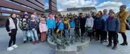 Grupowe zdjęcie wszystkich dzieci uczestniczących w wycieczce do Narodowego Forum Muzyki we Wrocławiu 12 kwietnia 2023 r. w tle widoczny budynek NFM
