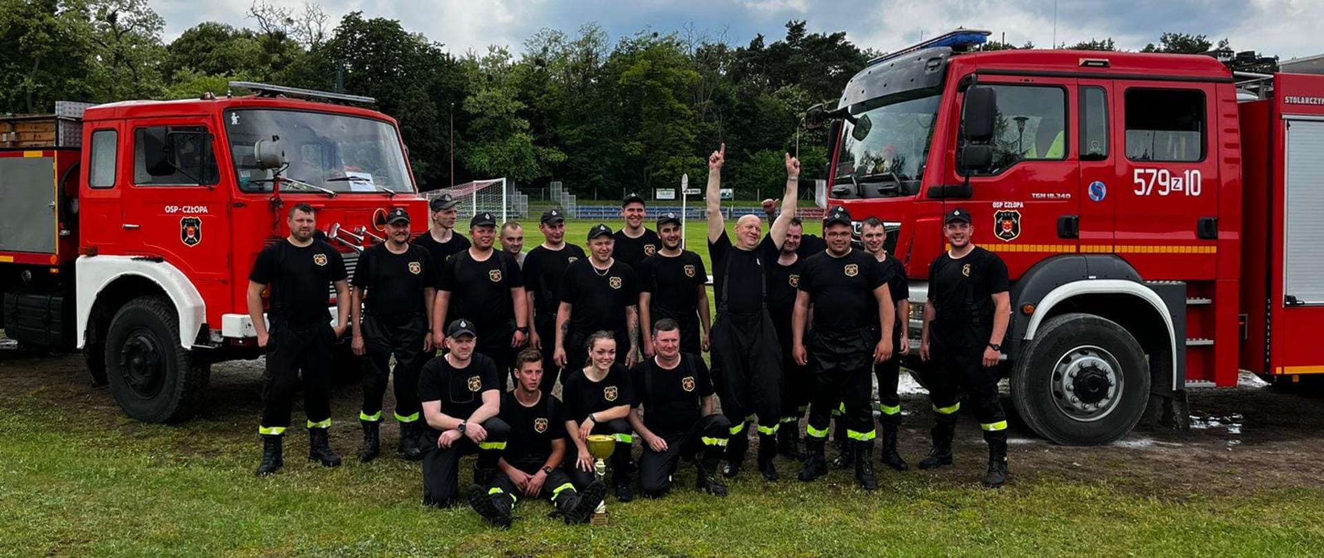 Zdjęcie przedstawia druhów OSP Człopa, zwycięscy gminnych zawodów sportowo–pożarnicze jednostek OSP Człopa 2022 na tle samochodów pożarniczych