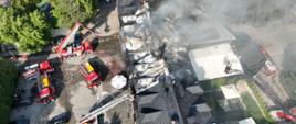 Widok z lotu ptaka. W centrum widać zniszczony pożarem dach hotelu, widać ogień i dym. Dookoła budynku znajdują się wozy strażackie