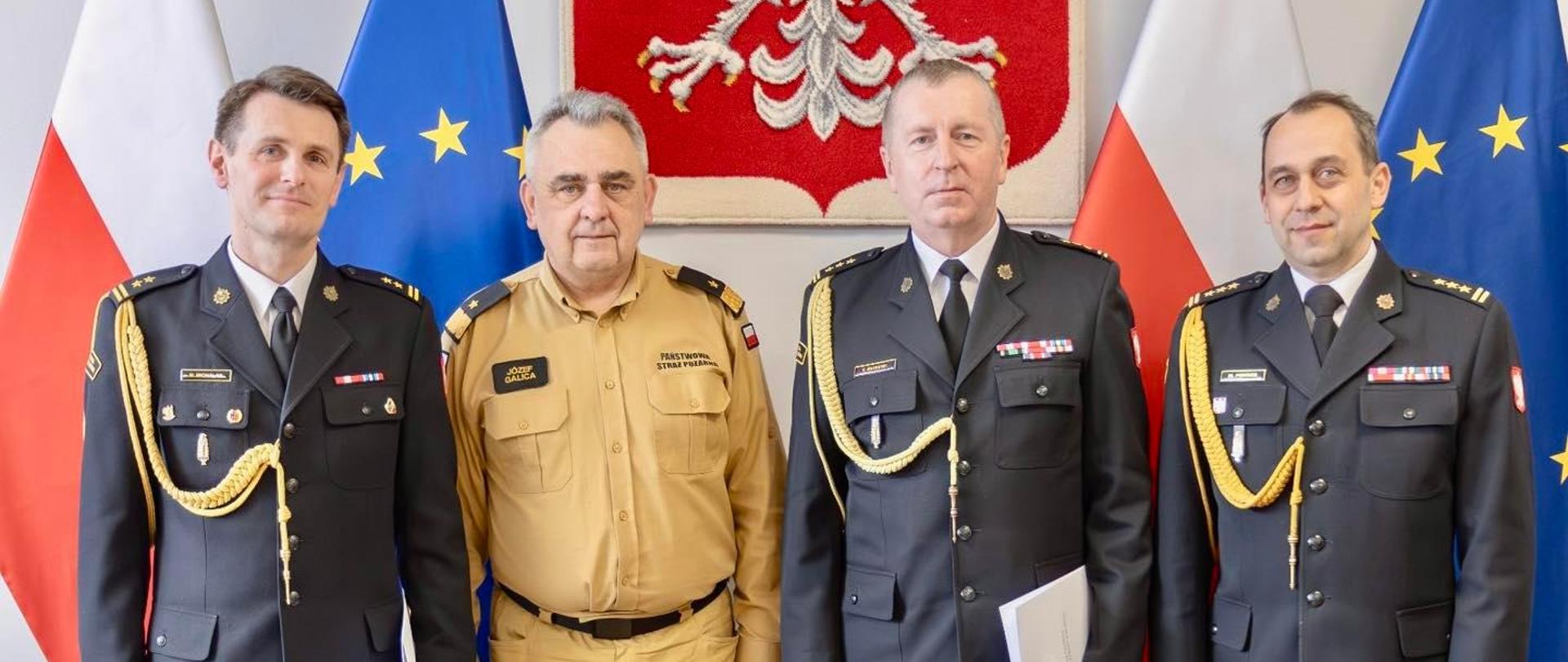 Od lewej stoją w kolejności zastępca zachodniopomorskiego komendanta wojewódzkiego PSP, zastępca komendanta głównego PSP, drugi zastępca zachodniopomorskiego komendanta wojewódzkiego PSP oraz zachodniopomorski komendant wojewódzki PSP. Za osobami na fotografii widoczne godło Polski oraz flagi Polski i Unii Europejskiej.