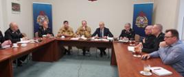 Na zdjęciu widzimy zespół roboczy podczas spotkania w składzie min. Zachodniopomorski Komendant Wojewódzki PSP st. bryg. Jarosław Tomczyk, zastępca Zachodniopomorskiego Komendanta Wojewódzkiego PSP st. bryg. Marek Popławski, Naczelnik Wydziału Kwatermistrzowskiego Komendy Wojewódzkiej PSP w Szczecinie st. bryg. Sylwester Podwyszyński, prezes Zarządu Wojewódzkiego Związku OSP RP dh Marek Kowalski wraz z zespołami. Siedzą przy brązowym stole konferencyjnym. W tle kremowa ściana oraz banery PSP 