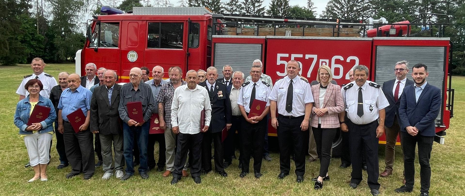 Wspólne zdjęcie druhów OSP wraz z Komendantem Powiatowym na tle samochodu pożarniczego.
