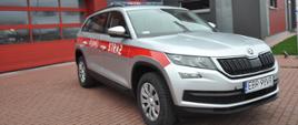 Na zdjęciu samochód lekki operacyjny marki Skoda Kodiaq na tle Komendy powiatowej PSP w Brzezinach. Samochód koloru srebrnego z oznaczeniami STRAŻ oraz numerem operacyjnym 410E91. Przód pojazdu 