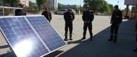Na zdjęciu trenażer fotowoltaiczny podczas prezentacji, ponadto wokół trenażera 5 strażaków w ubraniu koszarowym