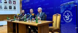 Minister Wieczorek i dwóch mężczyzn w garniturach siedzą za drewnianym stołem, za nimi niebieska ścianka z napisem Uniwersytet Szczeciński.