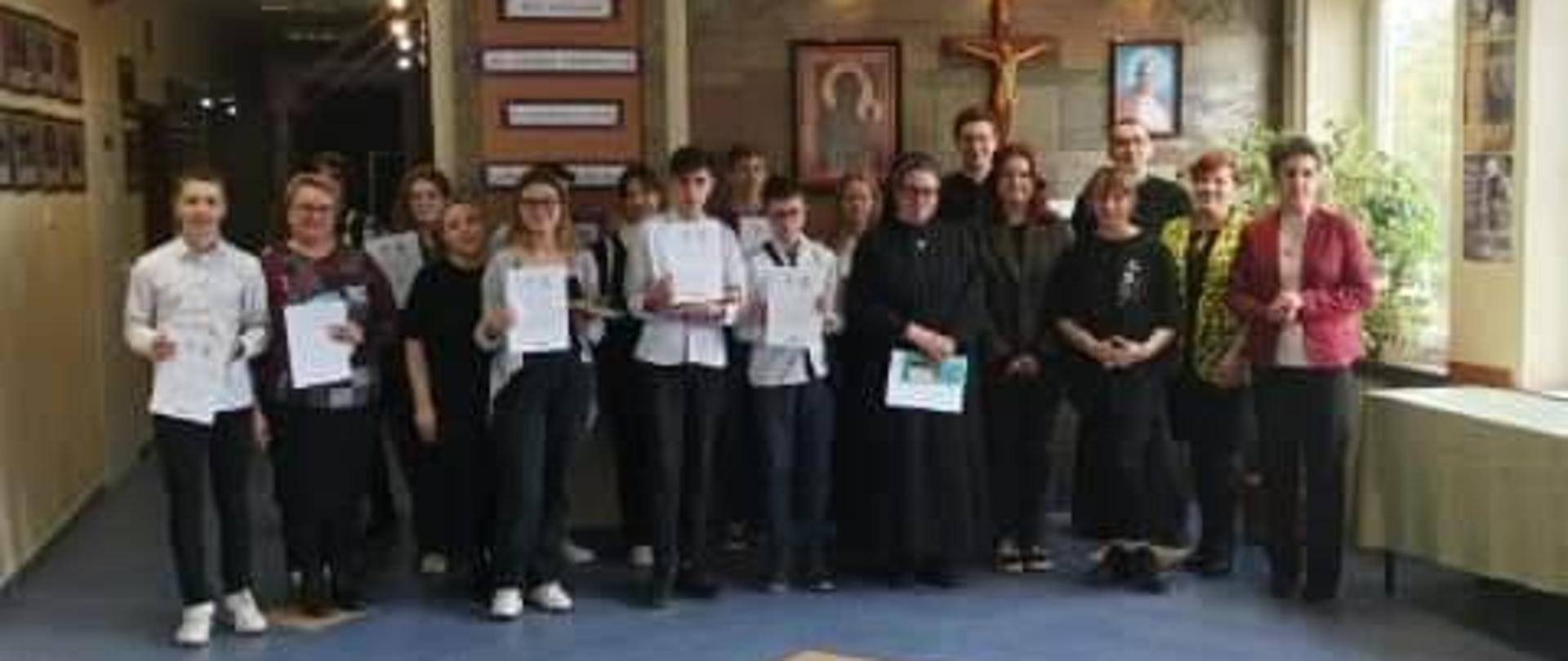Zdjęcie uczestników Powiatowego Konkursu Biblijnego w korytarzu Zespołu Szkół Katolickich w Piszu. Laureaci trzymają dyplomy.