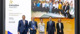 Andrzej Domański, minister finansów i gospodarki, Marcin Łoboda, szef Krajowej Administracji Skarbowej, oraz przedstawiciele Urzędu Skarbowego w Staszowie prezentują dyplom i statuetkę „Gwiazda Jakości”. Na ekranie w tle widoczna jest nazwa urzędu, zdjęcie zespołu oraz fragmenty opinii klientów.
