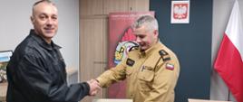 Komendant Powiatowy Państwowej Straży Pożarnej w Człuchowie st. bryg. Radosław Batruch stoi w gabinecie i wręcza akt mianowania st. ogn. Rafałowi Grubak na stanowisko młodszy operator sprzętu.