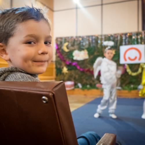 dziecko siedzi na fotelu, w tle inne dzieci choinki oraz logo Polskiej pomocy