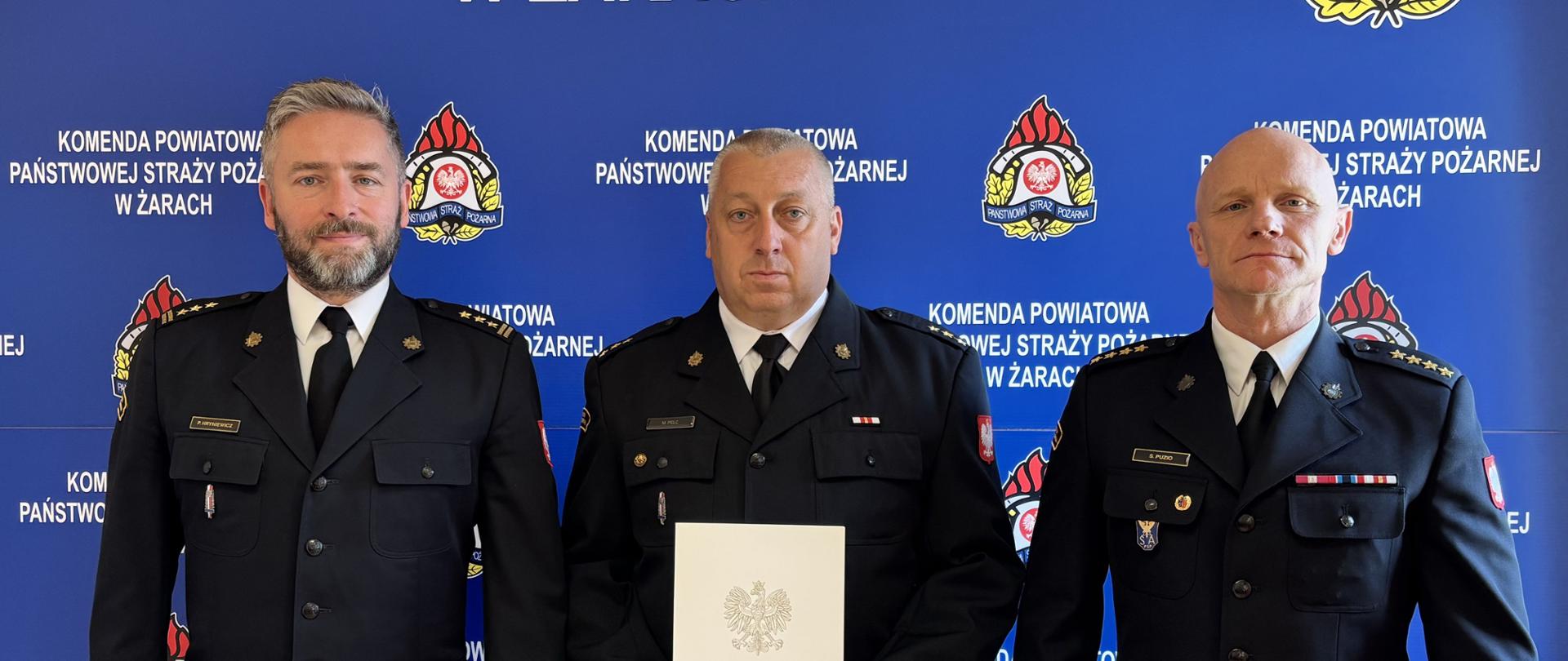 Na zdjęciu widoczny jest strażak otrzymujący nagrodę z Komendantem i Dowódcą JRG 