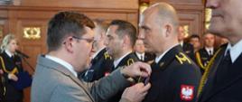 Zdjęcie przedstawia moment wręczenia odznaczenia przez II Wice Wojewodę Zachodniopomorskiego Mateusza Wagemann dla st. ogn. Marcina Praźmo