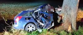 Nocna pora, niebieski samochód osobowy ze zniszczona karoserią w wyniku uderzenia w drzewo od strony pasażera. Oba skrzydła drzwiowe otwarte