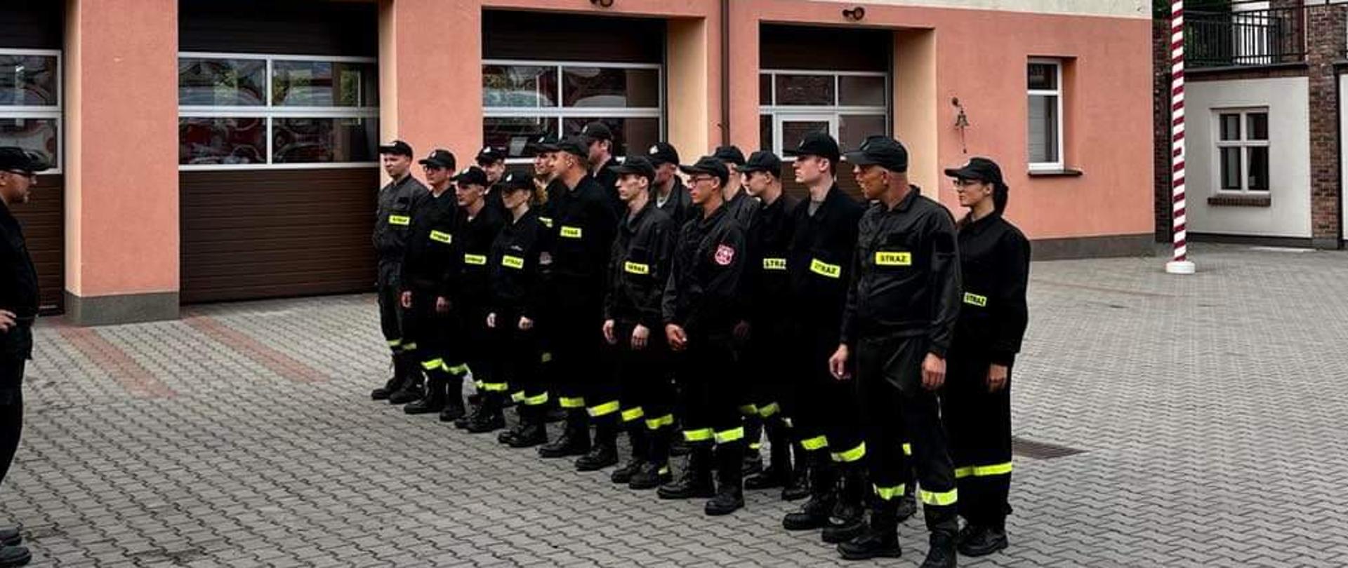 Na zdjęciu widać strażaków na zakończeniu szkolenia podstawowego strażaka ratownika Ochotniczych Straży Pożarnych. Strażacy ubrani w czarne umundurowanie koszarowe.