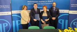 4 osoby na tle banneru w kolorze niebieskim z logo i napisem Państwowa Inspekcja Pracy. Od lewej strony: Pani Małgorzata Kruszewska Kierownik Oddziału Higieny Pracy i Nadzoru Nad Chemikaliami w Wojewódzkiej Stacji Sanitarno-Epidemiologicznej w Białymstoku, p.o. Okręgowego Inspektora Pracy w Białymstoku dr. Karol Łapiński, dr n. med. Maria Siewko – Podlaski Państwowy Wojewódzki Inspektor Sanitarny w Białymstoku , Pan Tomasz Werdoni p.o. Zastępca Okręgowego Inspektora Pracy ds. Nadzoru w Białymstoku 