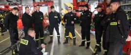 Strażacy stoją w garażu komendy nad rozłożonym sprzętem ratowniczym i słuchają wykładu.
