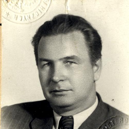 Adam Rapacki czarno-biały portret mężczyzny, ciemne włosy, ciemna marynarka, ciemny krawat, biała koszula.