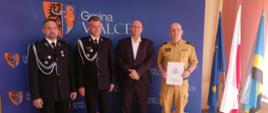 Na tle ścianki - bannera promocyjnego Gminy Walce w kolorze niebieskim z herbem Walec ustawieni sygnatariusze porozumienia: od lewej naczelnik OSP Walce, prezes OSP Walce, wójt Walec i Komendant Powiatowy PSP w Krapkowicach. Strażacy OSP w mundurach galowych, wójt Walec w ciemnym garniturze, Komendant Powiatowy PSP w umundurowaniu służbowym koloru piaskowego. Po prawej stojak z flagami : Polski, Gminy Walce i UE. 