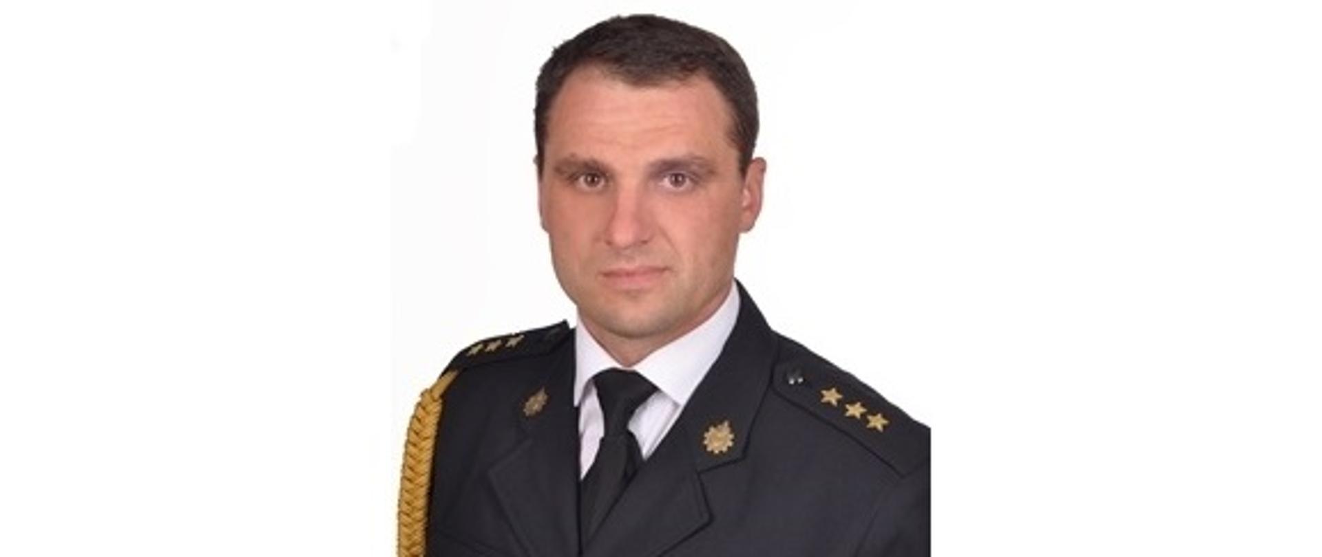 Zdjęcie portretowe zastępcy komendanta kapitana Krzysztofa Juszczaka na białym tle w mundurze galowym.