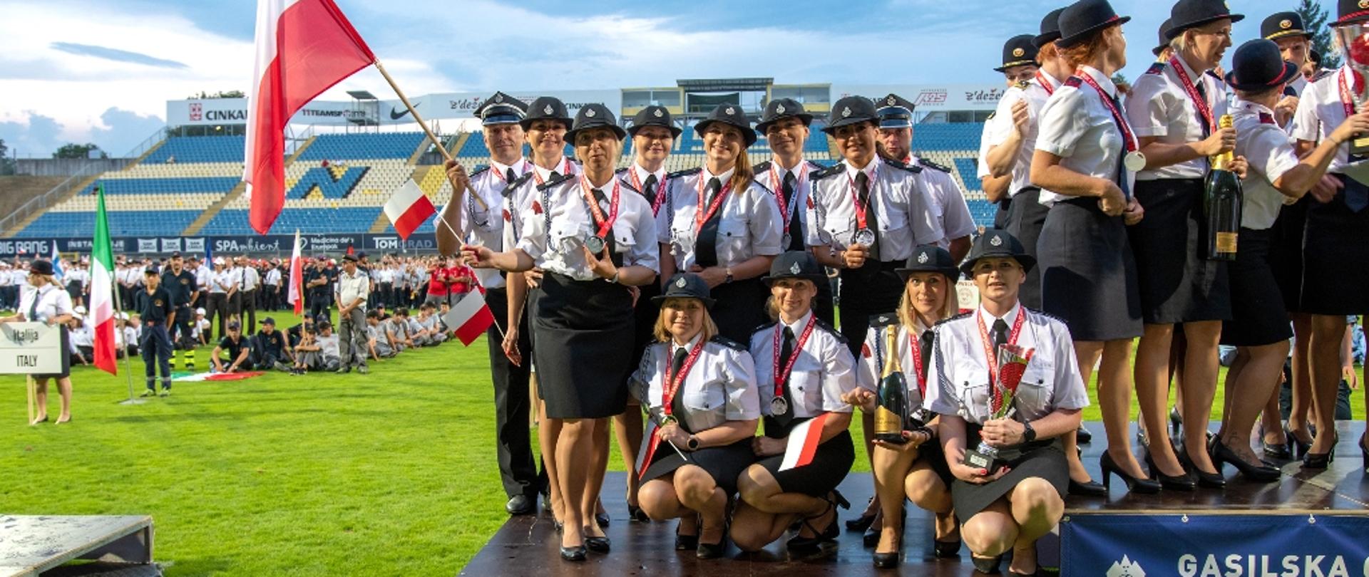 Drużyna żeńska OSP Lądek na drugim stopniu podium, wydarzenie na płycie stadionu. 