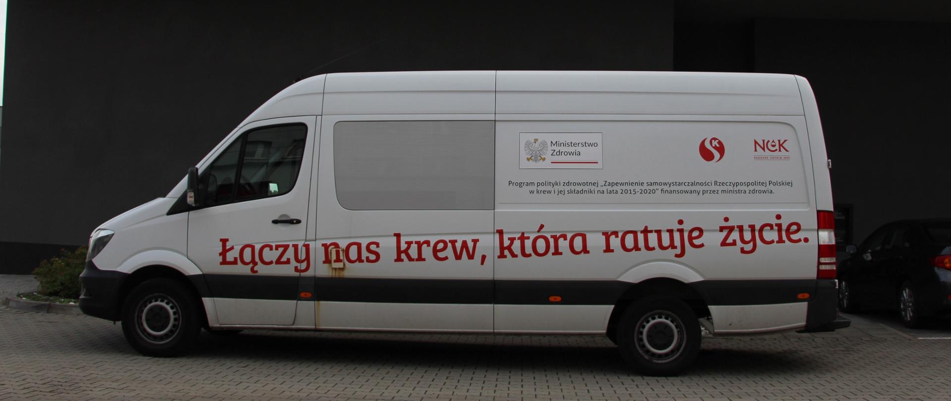 Zdjęcie przedstawia mobilny punkt pobrań krwi na tle budynku jednostki ratowniczo-gaśniczej.